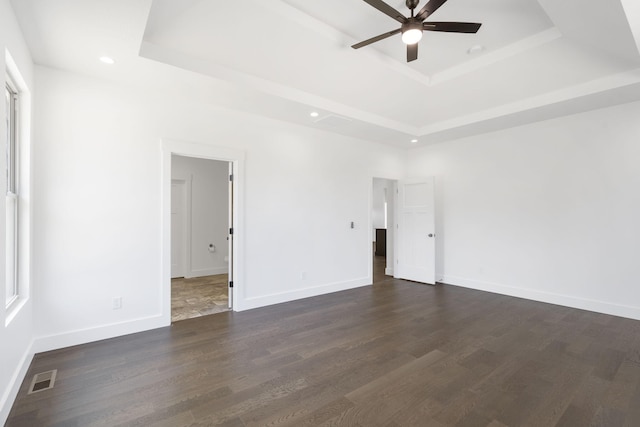 unfurnished room with a raised ceiling, ceiling fan, and dark wood-type flooring