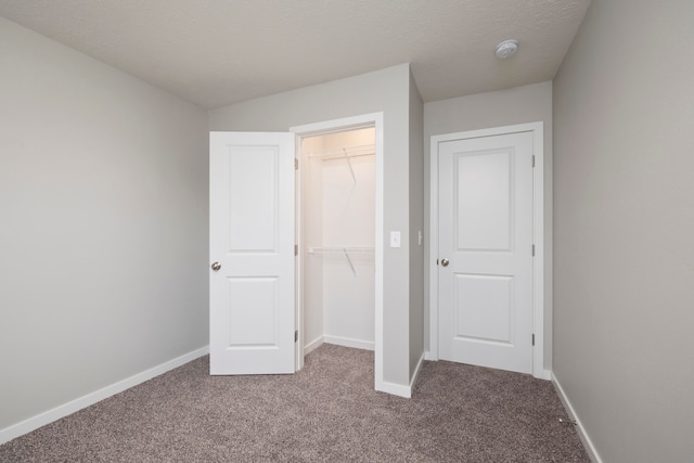 unfurnished bedroom with a textured ceiling, a closet, carpet, and a walk in closet