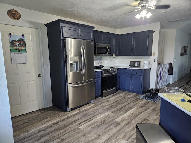 kitchen featuring ceiling fan, blue cabinets, a textured ceiling, appliances with stainless steel finishes, and light wood-type flooring