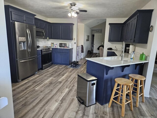 kitchen featuring light hardwood / wood-style floors, a breakfast bar, stainless steel appliances, kitchen peninsula, and a textured ceiling