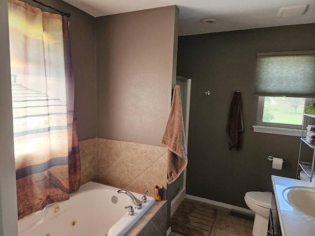 bathroom with tiled tub, vanity, tile patterned flooring, and toilet