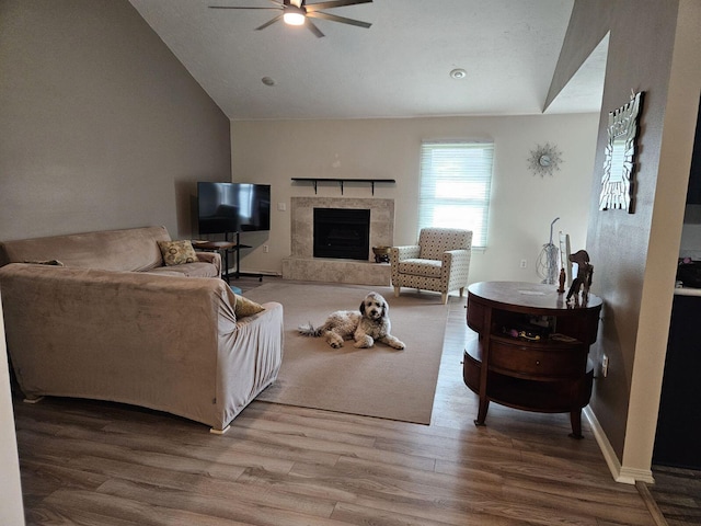 living room with wood-type flooring, ceiling fan, vaulted ceiling, and a tile fireplace