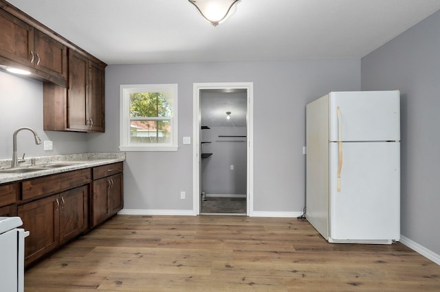 kitchen with white fridge, dark brown cabinets, sink, and light hardwood / wood-style floors