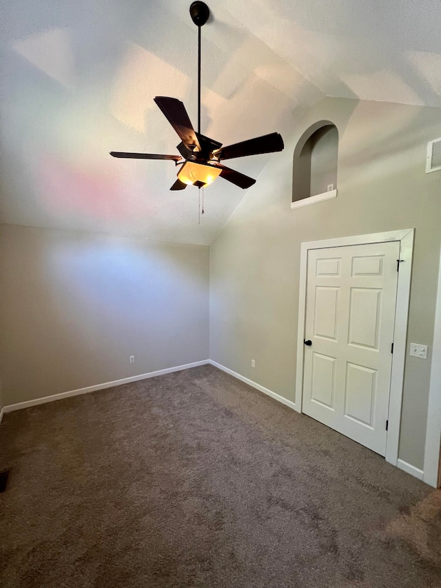 spare room featuring dark carpet, vaulted ceiling, and ceiling fan