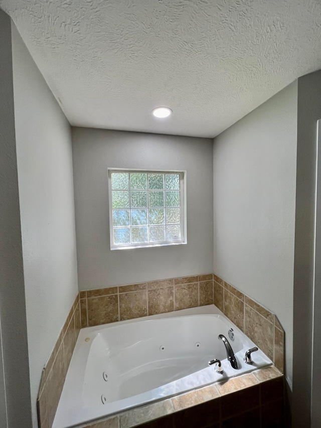 bathroom with tiled bath and a textured ceiling