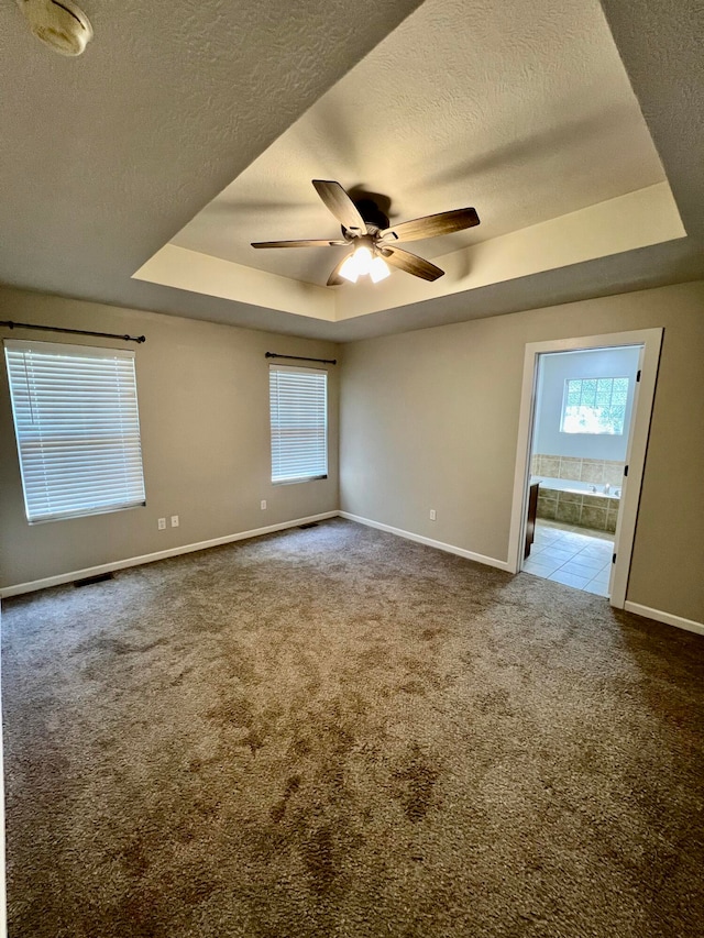 empty room featuring a raised ceiling, carpet flooring, and ceiling fan