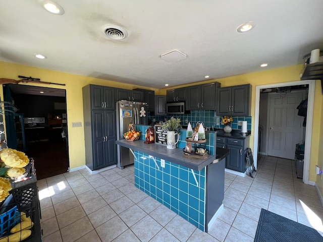 kitchen featuring light tile patterned flooring, appliances with stainless steel finishes, backsplash, and a center island