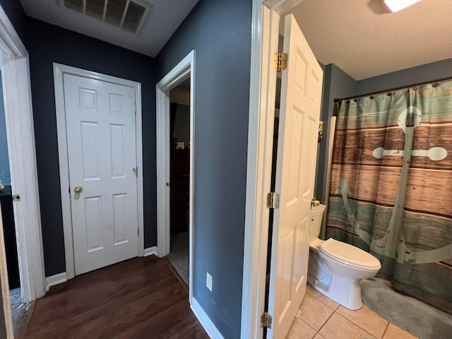 bathroom featuring hardwood / wood-style flooring, toilet, a shower with shower curtain, and a textured ceiling