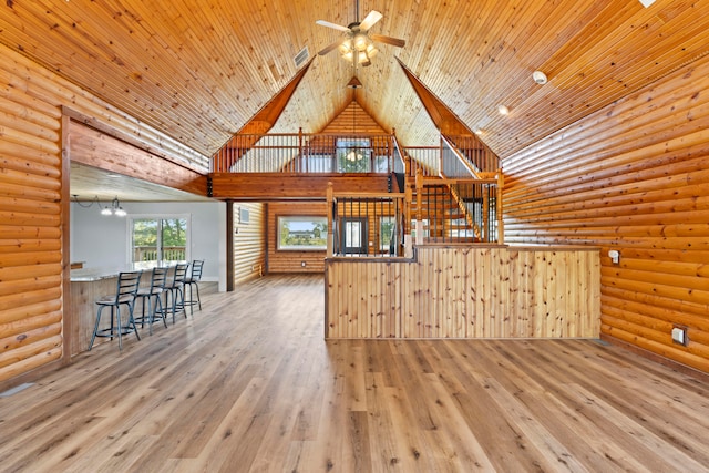 unfurnished living room with high vaulted ceiling, ceiling fan, wood-type flooring, wooden ceiling, and rustic walls