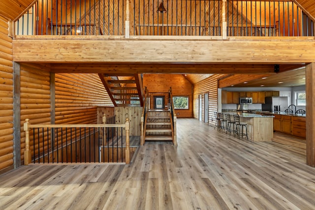 unfurnished living room featuring high vaulted ceiling, log walls, and light hardwood / wood-style flooring