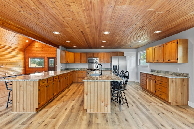 kitchen with an island with sink, light wood-type flooring, stainless steel appliances, and a kitchen breakfast bar