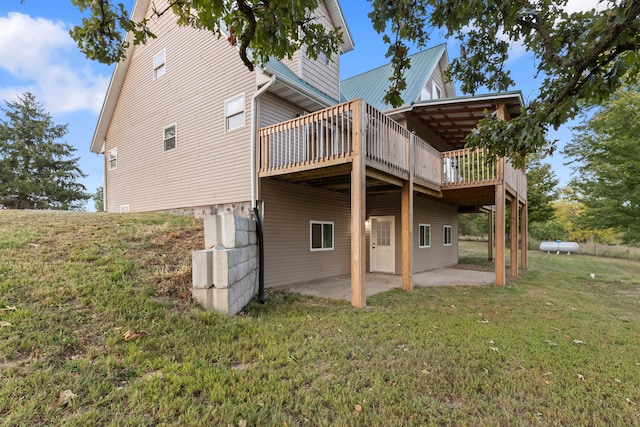 rear view of property featuring a wooden deck, a lawn, and a patio area