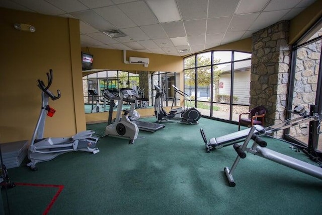 workout area featuring an AC wall unit, a drop ceiling, and carpet floors