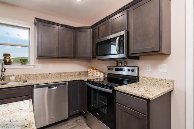 kitchen with light stone countertops, sink, stainless steel appliances, dark brown cabinetry, and light hardwood / wood-style flooring