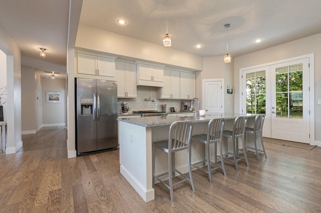 kitchen featuring light stone counters, stainless steel refrigerator with ice dispenser, a center island with sink, and white cabinetry