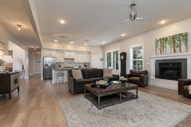 living room with ceiling fan, light wood-type flooring, and a tile fireplace