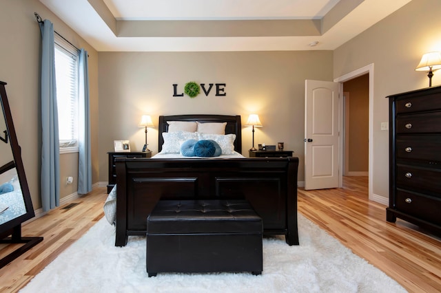 bedroom with light hardwood / wood-style flooring and a tray ceiling