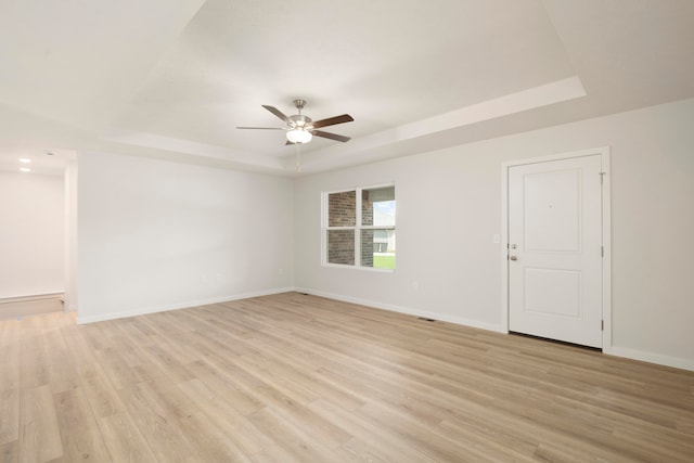 unfurnished room with light wood-type flooring, ceiling fan, and a raised ceiling