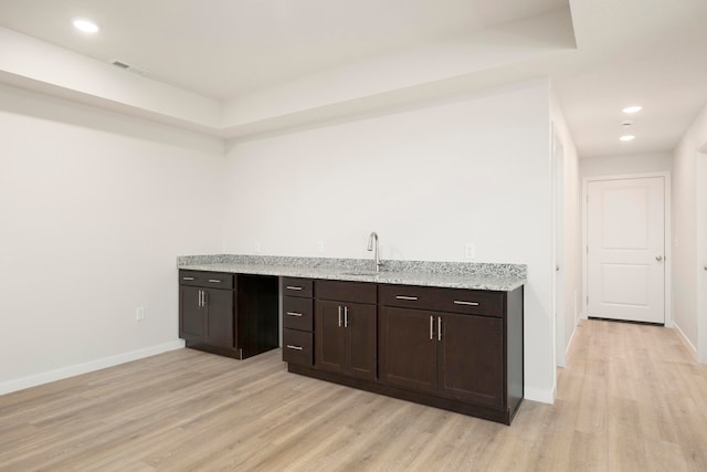 bar with sink, light stone counters, light wood-type flooring, and dark brown cabinets