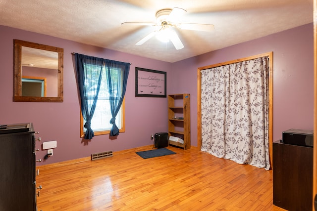 exercise area featuring ceiling fan, light hardwood / wood-style floors, and a textured ceiling