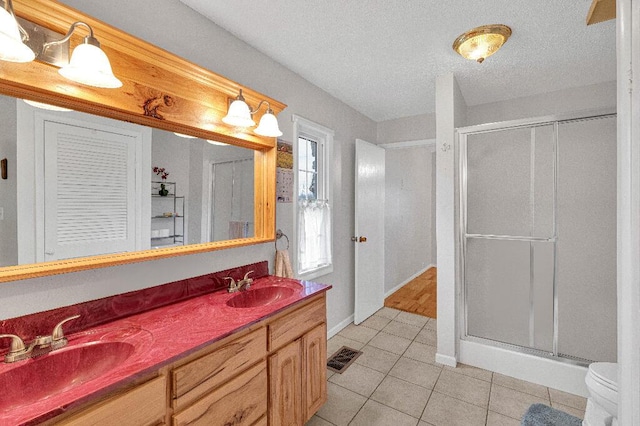 bathroom with tile patterned floors, vanity, a textured ceiling, a shower with door, and toilet