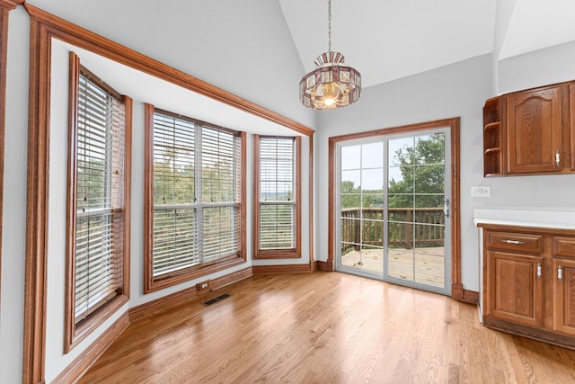 unfurnished dining area featuring light wood-type flooring, vaulted ceiling, baseboards, visible vents, and a chandelier