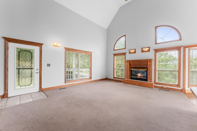 unfurnished living room featuring baseboards, a glass covered fireplace, carpet floors, and high vaulted ceiling