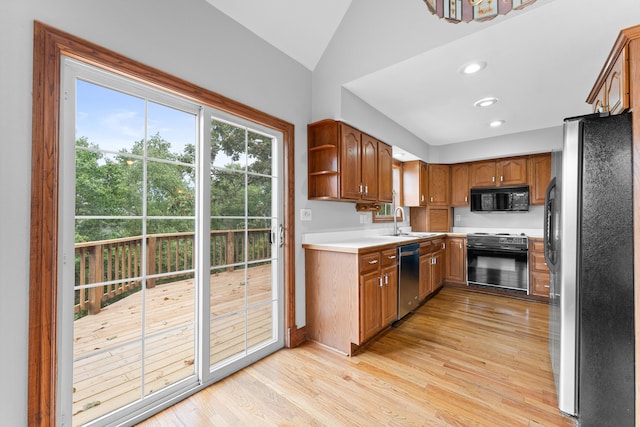 kitchen featuring black appliances, vaulted ceiling, sink, and light hardwood / wood-style floors