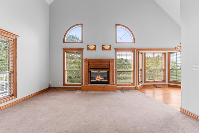 unfurnished living room with a glass covered fireplace, baseboards, carpet flooring, and high vaulted ceiling