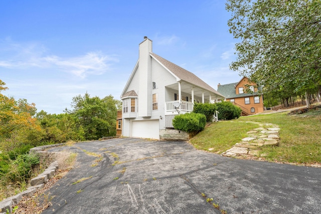 view of property exterior with a chimney, aphalt driveway, covered porch, a lawn, and a garage
