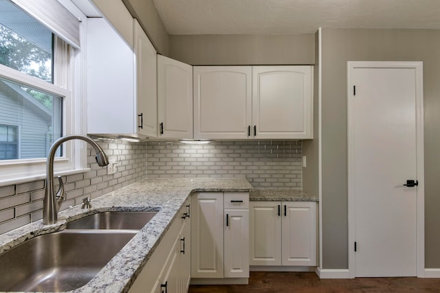 kitchen with backsplash, sink, light stone counters, and white cabinetry