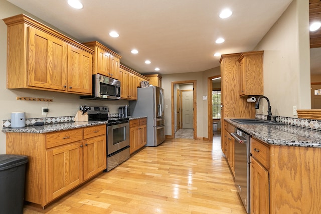 kitchen featuring appliances with stainless steel finishes, dark stone countertops, sink, and light hardwood / wood-style floors