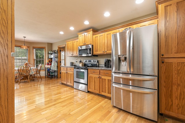 kitchen featuring decorative light fixtures, stainless steel appliances, stone countertops, and light hardwood / wood-style flooring