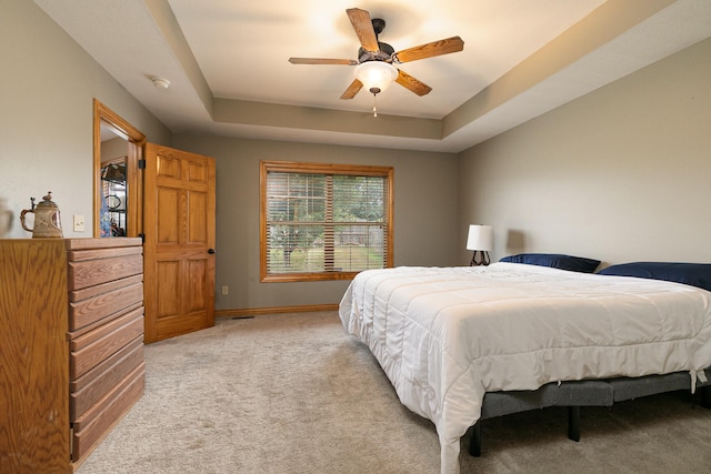 bedroom with light carpet, ceiling fan, and a tray ceiling