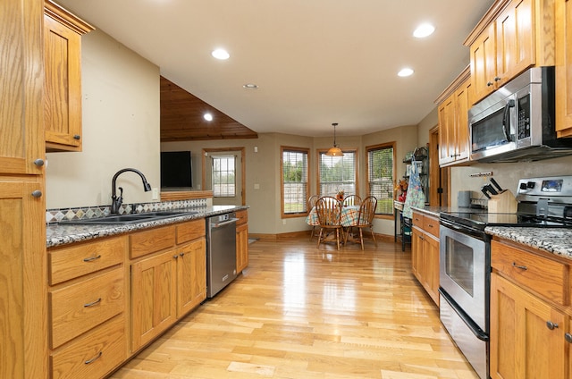 kitchen with hanging light fixtures, sink, light hardwood / wood-style flooring, appliances with stainless steel finishes, and light stone countertops