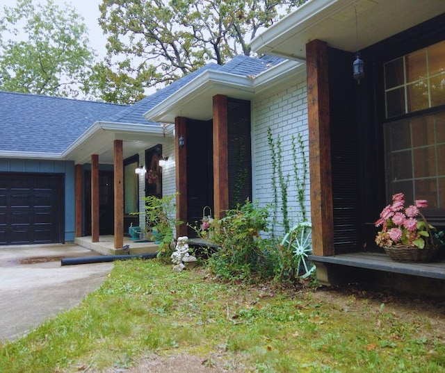 entrance to property with concrete driveway, a shingled roof, covered porch, a garage, and brick siding