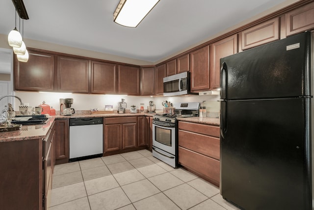 kitchen with light stone countertops, appliances with stainless steel finishes, hanging light fixtures, and light tile patterned floors