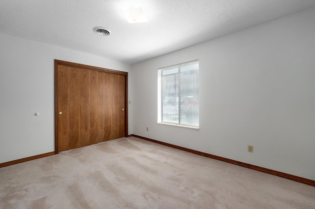 unfurnished bedroom with a closet, a textured ceiling, and light carpet