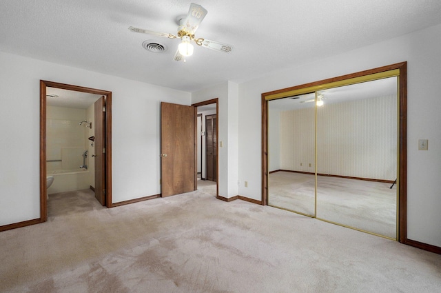 unfurnished bedroom featuring ceiling fan, light carpet, a closet, ensuite bath, and a textured ceiling