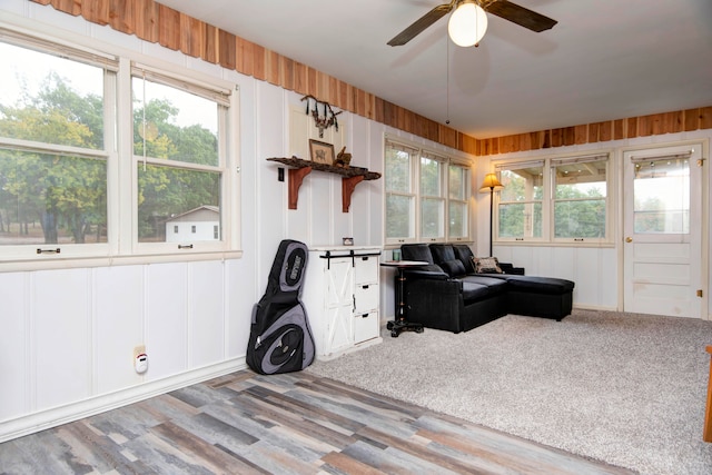 interior space with ceiling fan, hardwood / wood-style flooring, wood walls, and a healthy amount of sunlight