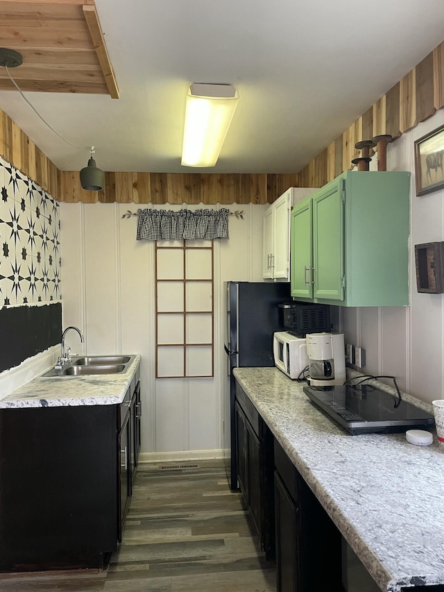 kitchen with wood-type flooring, sink, green cabinets, and wooden walls