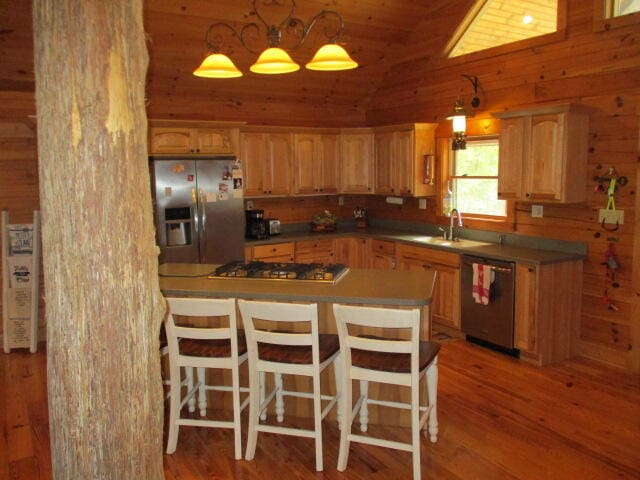 kitchen with hardwood / wood-style flooring, stainless steel appliances, wood walls, and vaulted ceiling