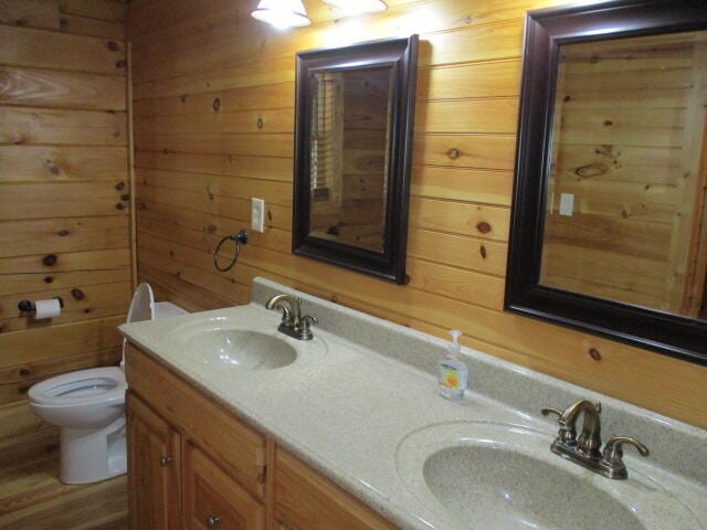 bathroom with hardwood / wood-style flooring, wooden walls, vanity, and toilet