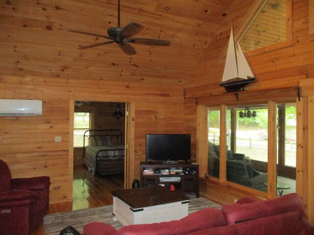 living room featuring wood-type flooring, plenty of natural light, high vaulted ceiling, and a wall unit AC