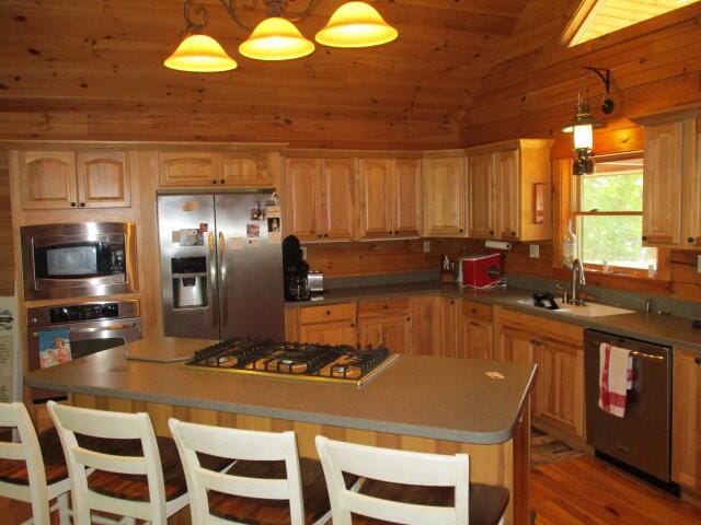 kitchen featuring lofted ceiling, hanging light fixtures, sink, a kitchen island, and stainless steel appliances