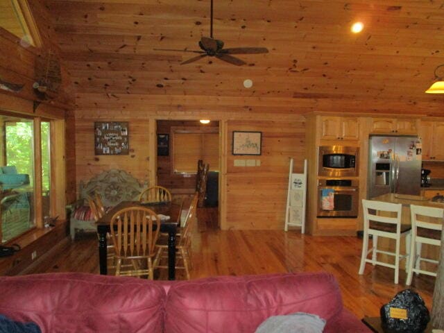 living room featuring wood walls, high vaulted ceiling, hardwood / wood-style floors, and ceiling fan