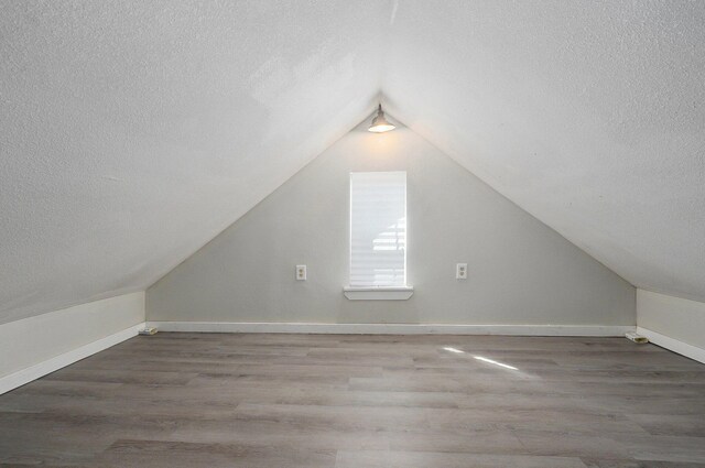 additional living space featuring lofted ceiling, hardwood / wood-style floors, and a textured ceiling