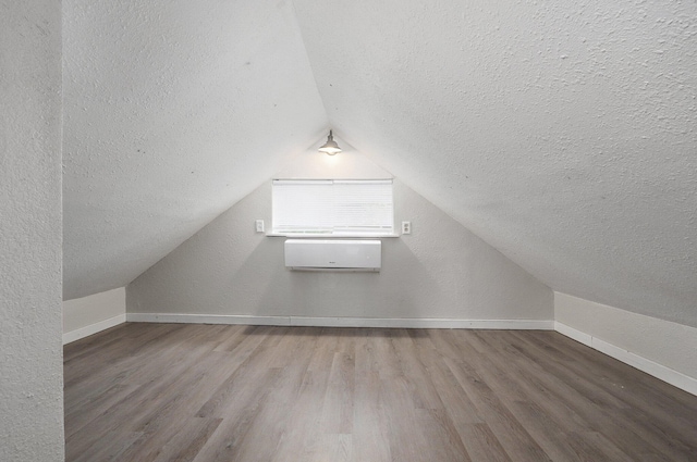 additional living space featuring lofted ceiling, a wall unit AC, wood-type flooring, and a textured ceiling