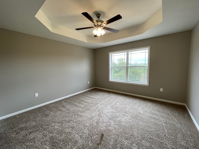 carpeted empty room featuring ceiling fan and a raised ceiling