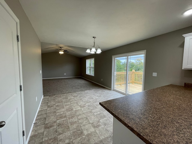 unfurnished dining area featuring ceiling fan with notable chandelier, vaulted ceiling, and light carpet